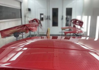 Nahaufnahme einer roten Hochglanz-Lackierung an Fahrzeugteilen in der Lackierkabine von Dr. Car Heilbronn, die die perfekte Spiegelung und Qualität der Arbeit zeigt.