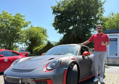 Geschäftsinhaber von Dr. Car Heilbronn steht neben einem mattgrauen Porsche 911 GT3 RS mit roten Akzenten und gibt ein „Daumen hoch“-Zeichen nach einer perfekten Runde auf dem Nürburgring