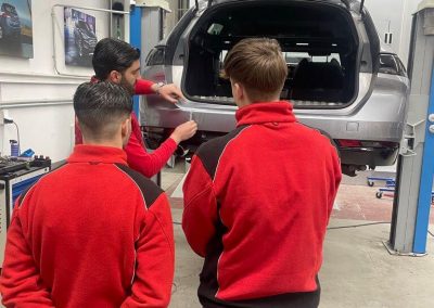 Das Team von Dr. Car in Heilbronn im Wissensaustausch während der Arbeit an einem grauen SUV-Heck in der Kfz-Werkstatt.
