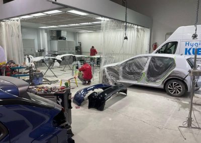 Blick in die großräumige Werkshalle von Dr. Car in Heilbronn mit mehreren Fahrzeugen in der Karosserie-Instandsetzung und Lackiervorbereitung.