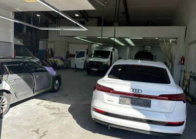 Blick in die Dr. Car Lackiererei in Heilbronn mit verschiedenen Fahrzeugen, darunter ein weißer Audi e-tron und ein Mercedes Sprinter zur Karosserieinstandsetzung