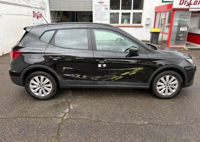 Ein schwarzer SEAT Arona mit deutlichem seitlichen Lackschaden (Streifschaden) und gelben Abriebspuren steht vor der Kfz-Lackiererei Dr. Car in Heilbronn zur Reparatur.