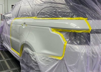 Seitenansicht eines Range Rover Geländewagens in der Lackierkabine von Dr. Car Heilbronn, vorbereitet mit präziser Abklebung für eine professionelle Seitenlackierung.