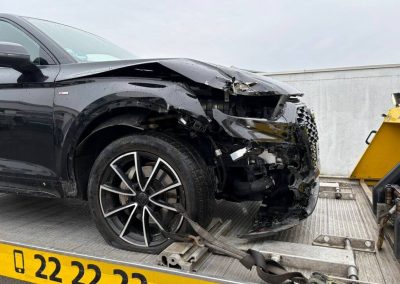 Stark beschädigter schwarzer Audi auf einem Abschleppanhänger vor der Dr. Car Werkstatt Heilbronn, bereit für die professionelle Unfallinstandsetzung.