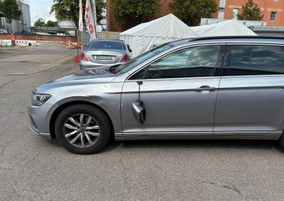 Silberner VW Passat mit abgerissenem Außenspiegel und Kratzern an der Fahrertür vor der Reparatur bei Dr. Car.